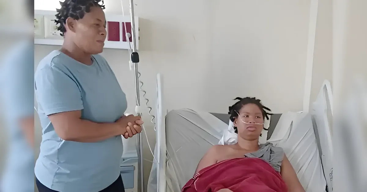 Caregiver standing beside a hospital bed with a patient who has a nasal oxygen tube and red blanket.