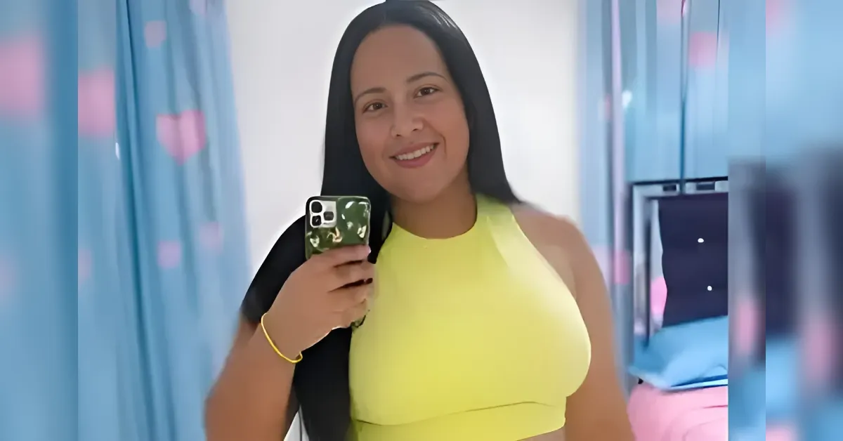 Smiling woman with long black hair in a bright yellow sleeveless top takes a selfie in a room, holding a phone with a green camouflage case.