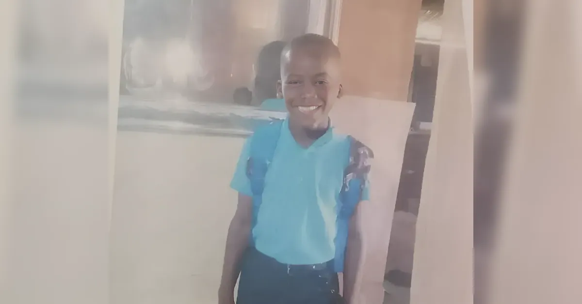 Smiling young person in a blue polo shirt with a backpack standing indoors.