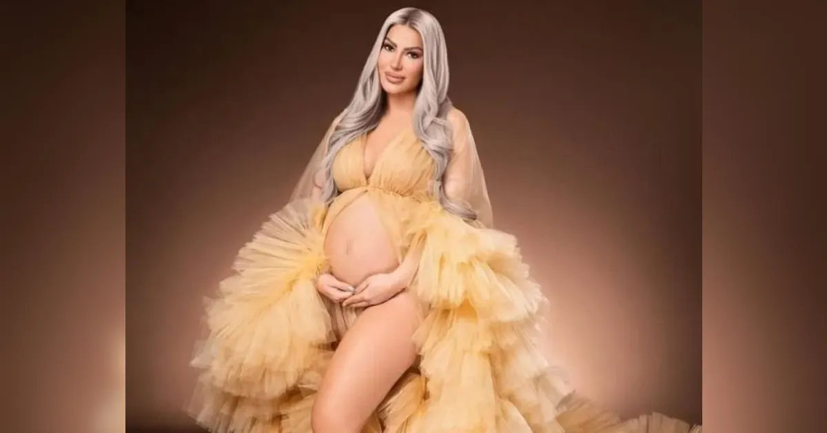 Pregnant woman wearing a voluminous yellow gown, cradling her baby bump with both hands.