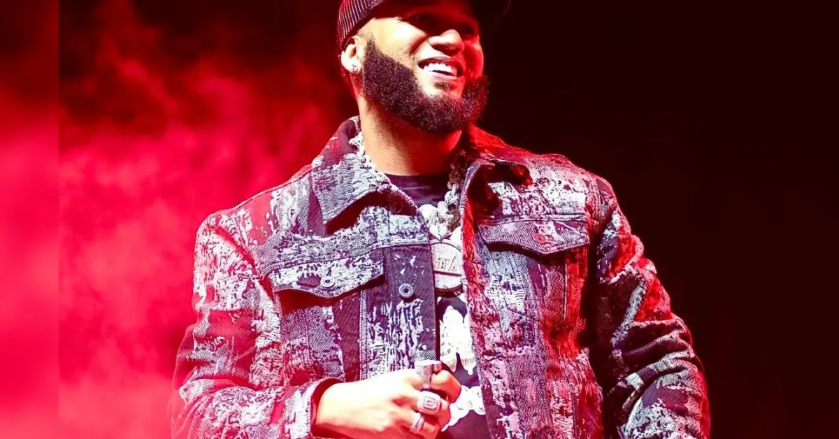 Male performer on stage smiling, wearing a distressed denim jacket under red stage lighting.