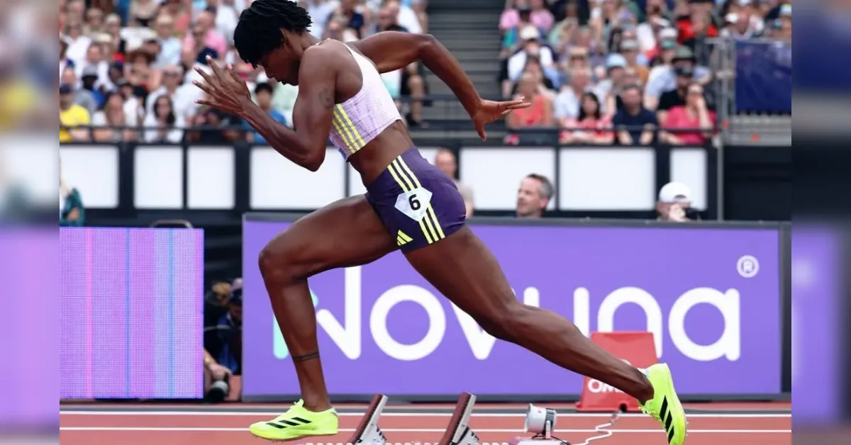 Male sprinter in a purple-yellow uniform explodes from starting blocks on a track, bib number 6, neon shoes, with a crowd in the stands behind.