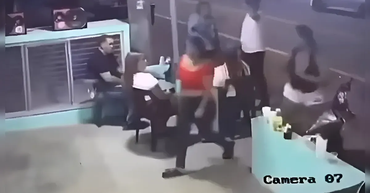 Indoor store scene with a turquoise counter; several customers stand nearby while a person sits behind the counter (surveillance footage).