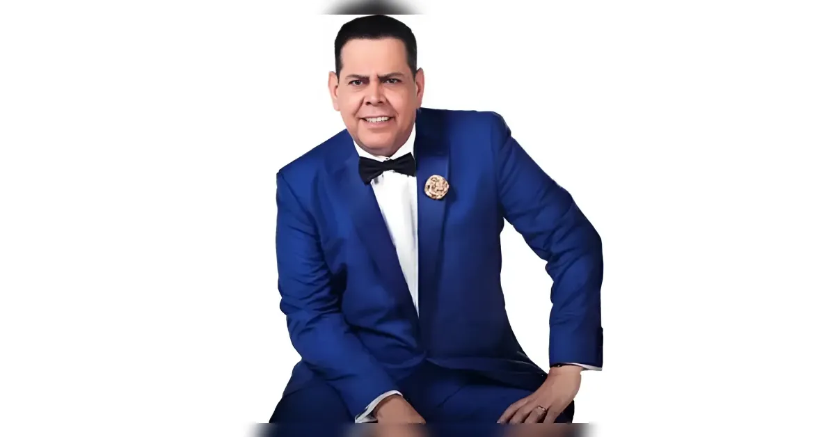 Man in a royal blue suit with a black bow tie, smiling, seated against a white studio background.