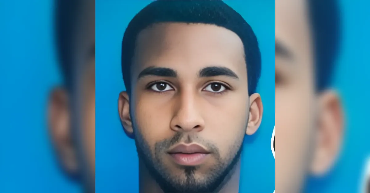 Close-up portrait of a young man with short dark hair and trimmed beard against a solid blue background.