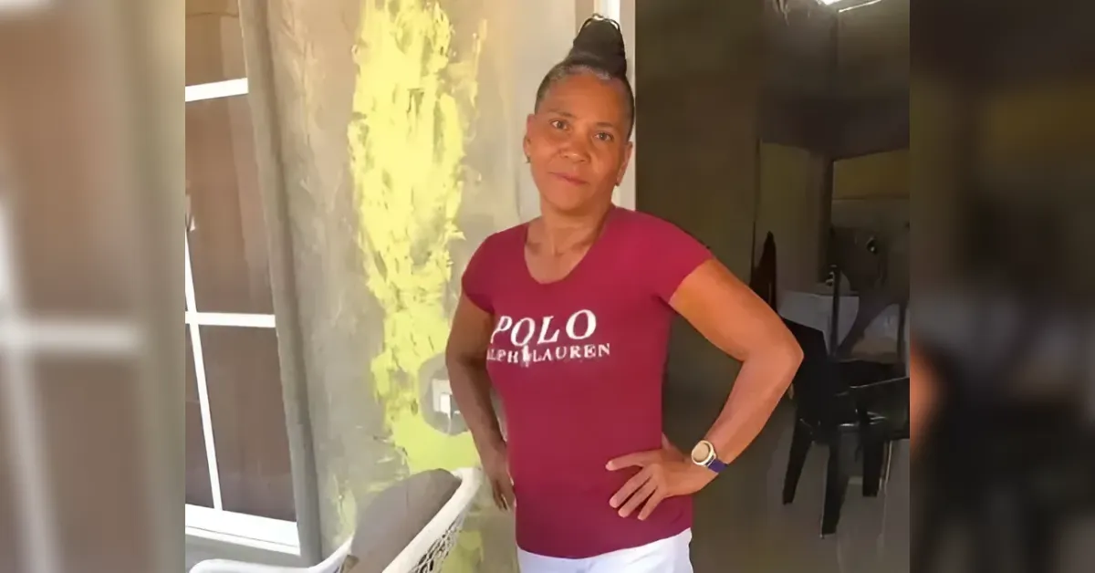 Woman standing with hands on hips, wearing a maroon Polo Ralph Lauren T-shirt and white pants, in a doorway area by a green wall.