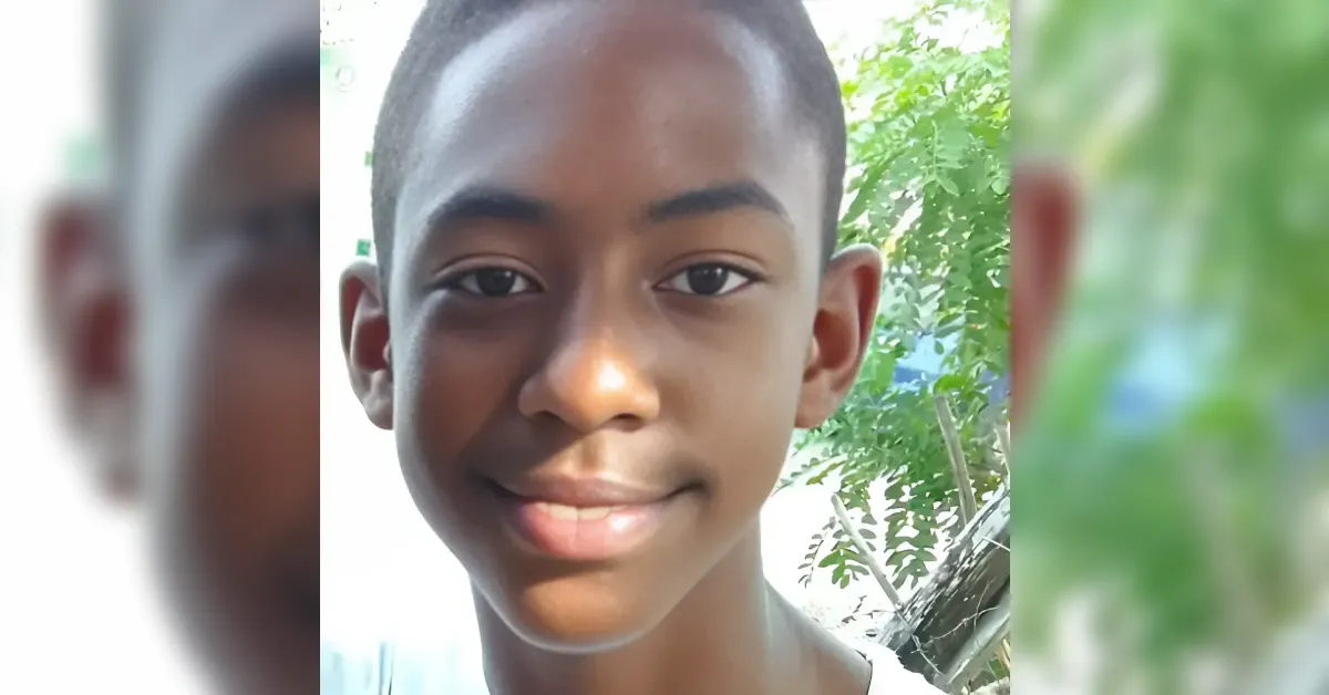 Close-up of a smiling boy outdoors with green trees in the background.
