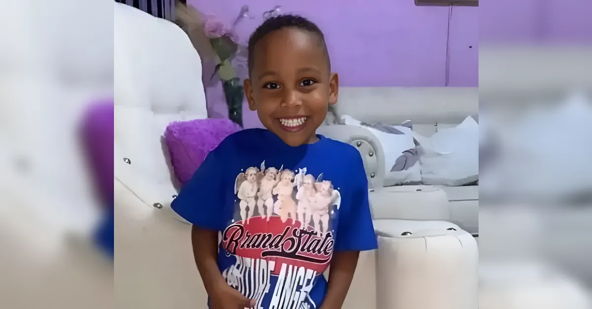 Smiling boy in a blue graphic t-shirt stands indoors in a room with purple decor neben a white sofa.