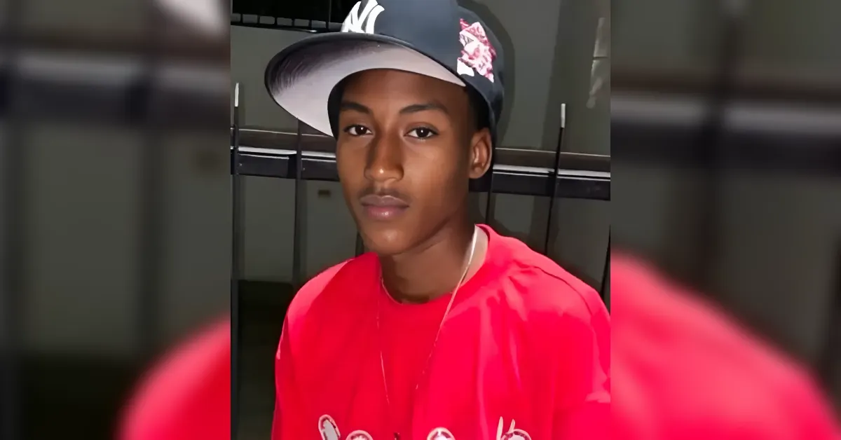Young person wearing a bright red shirt and a tilted black cap with a white brim, looking at the camera indoors.