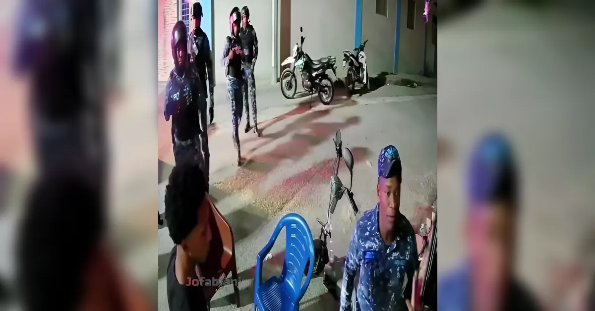 Group of armed men standing outside a building at night, with two motorcycles in the background near a wall.