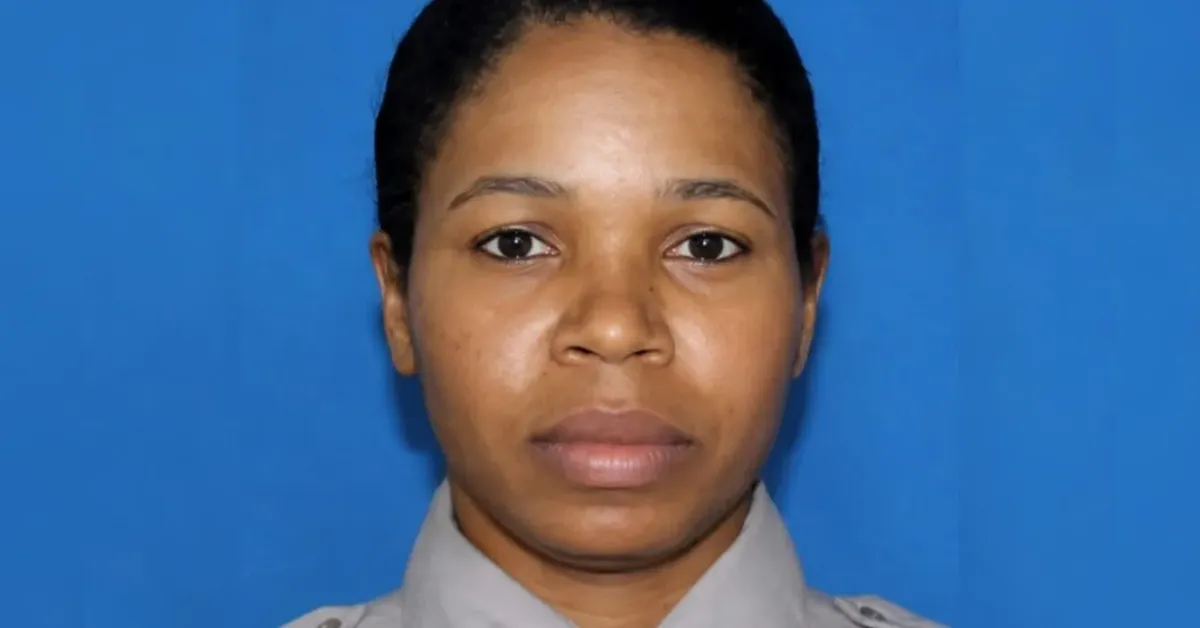 Front-facing head-and-shoulders portrait of a woman in a gray uniform against a solid blue background, neutral expression.