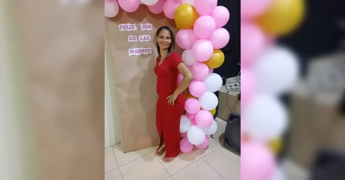Mujer con vestido rojo posando junto a un arco de globos rosas, blancos y amarillos en una celebración del Día de las Madres.