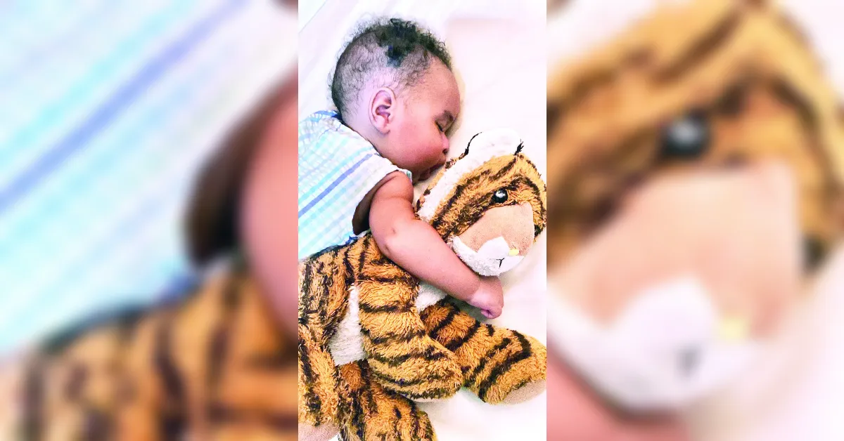 Baby asleep while cuddling a tiger stuffed animal on a white surface