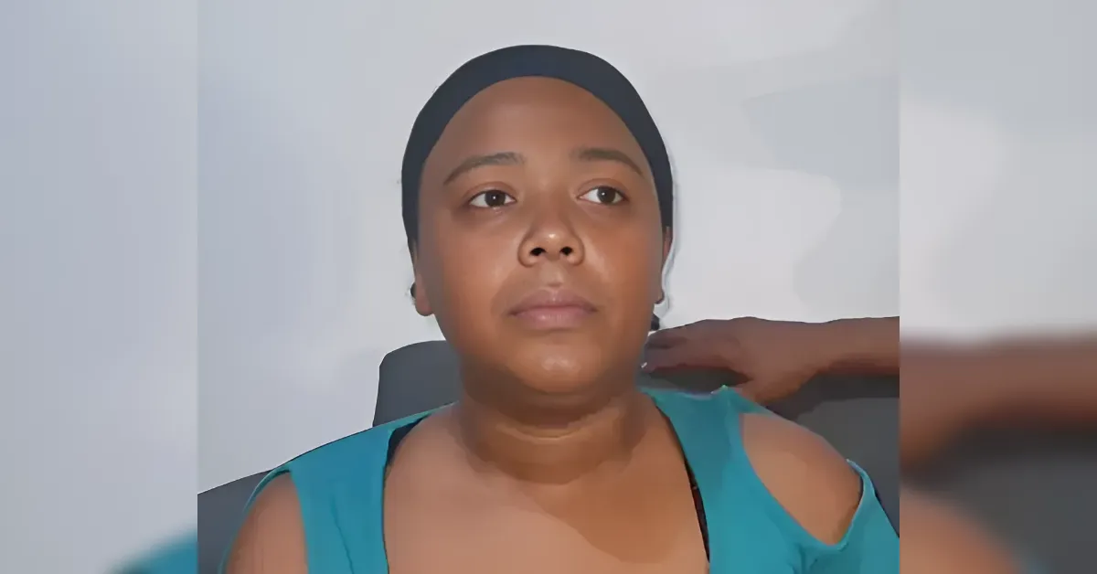 Woman in a teal sleeveless top and black headband sits against a light background with a neutral expression, looking forward.