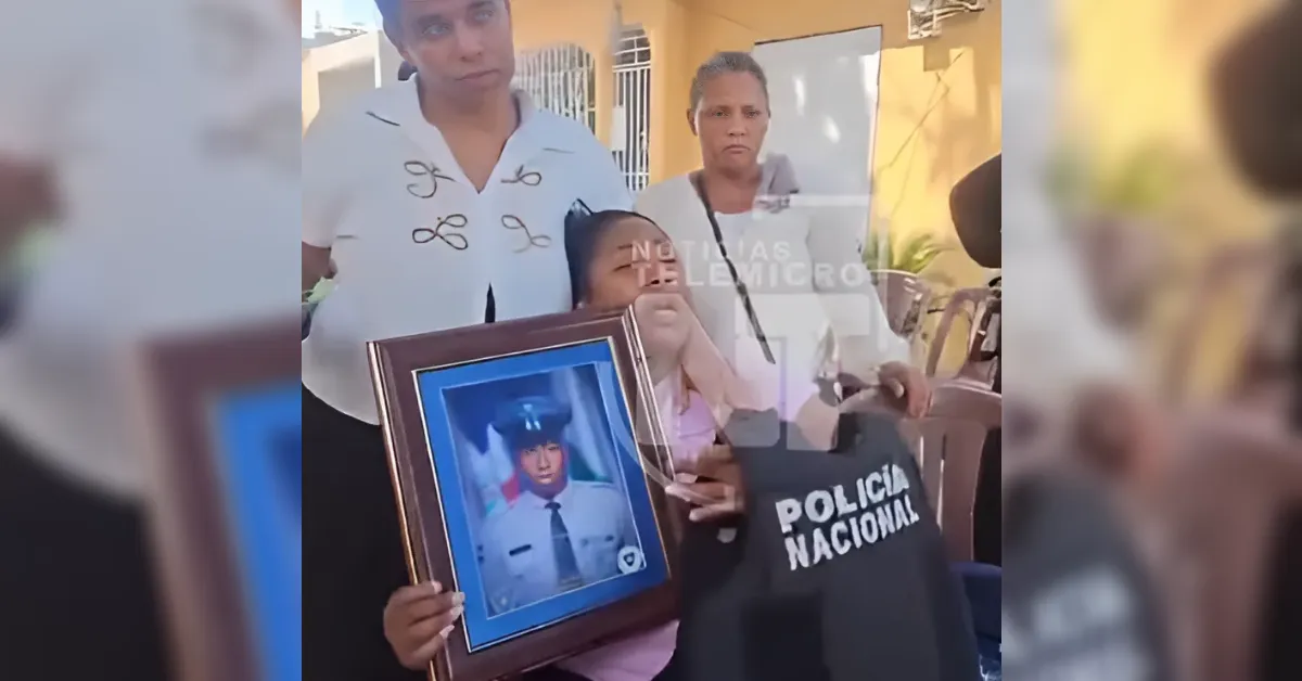 Grieving woman holding a framed photo of a uniformed police officer as others stand nearby; a black jacket with 'POLICIA NACIONAL' is visible in the foreground.