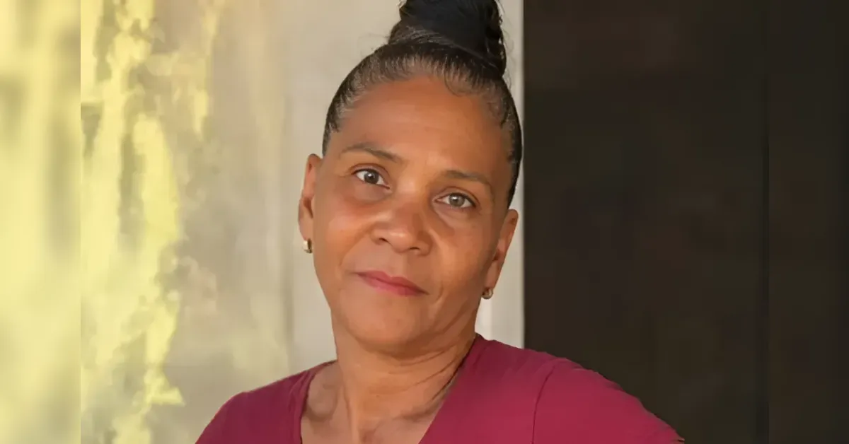 Woman with dark hair in a top bun, wearing a maroon shirt, looking at the camera with a gentle smile.