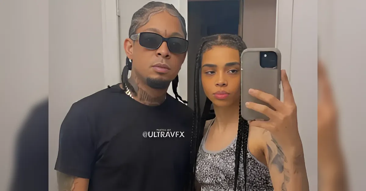 Couple posing for a mirror selfie: man in a black shirt and sunglasses, woman with braids and a sparkly top holding the phone.