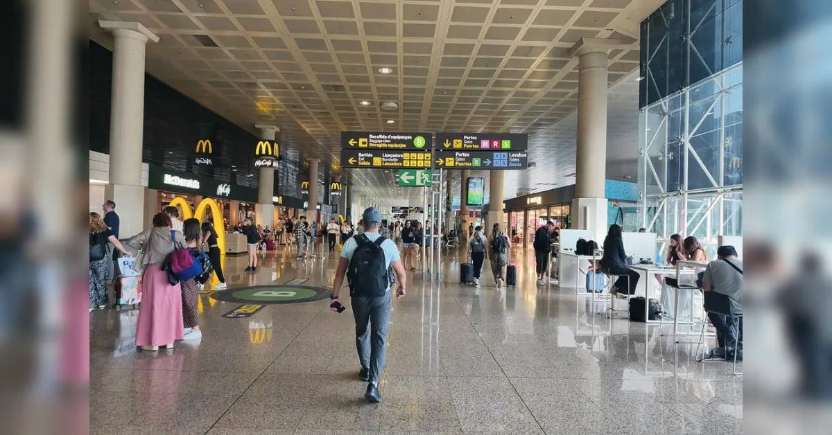 Busy airport terminal with a McDonald's on the left and travelers walking with luggage amid bright, polished floors and high ceilings.