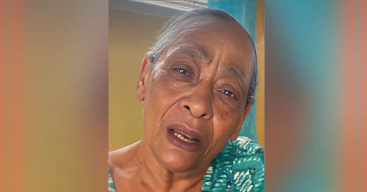 Close-up of an older woman with short gray hair, wearing a teal patterned top, looking at the camera with a calm, slightly concerned expression.
