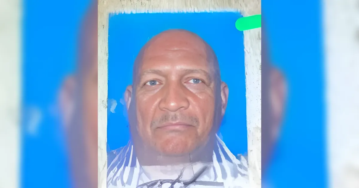 Close-up portrait of a middle-aged, bald man with a calm expression against a bright blue background.