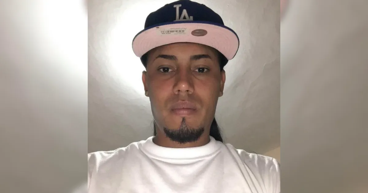 Portrait of a man wearing a navy and pink LA baseball cap and a white T-shirt, looking at the camera with a goatee.