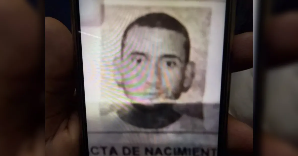 Smartphone screen showing a black-and-white portrait photo of a man, with partial text at the bottom suggesting a birth-related document (e.g., 'Acta de Nacimiento').