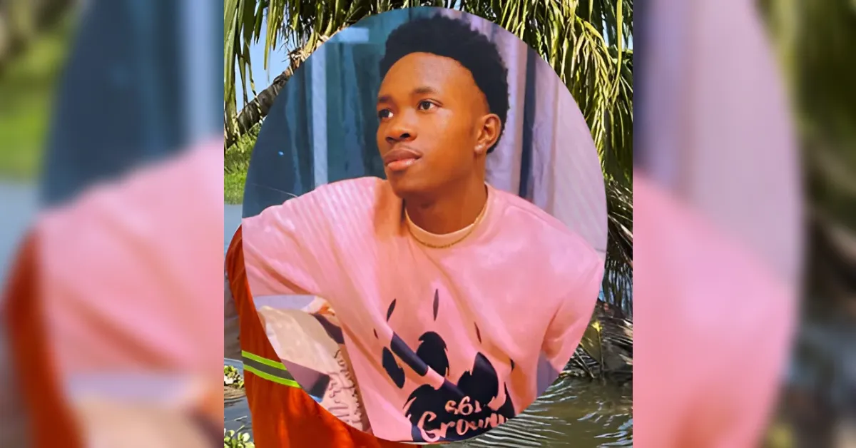 Portrait of a young man in a pink graphic T‑shirt, looking to the right, outdoors with palm trees in the background.