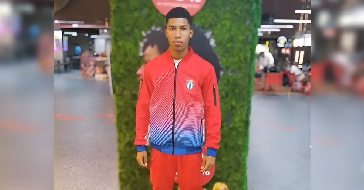 Young man in a red and blue gradient tracksuit posing in a mall with a green wall backdrop.