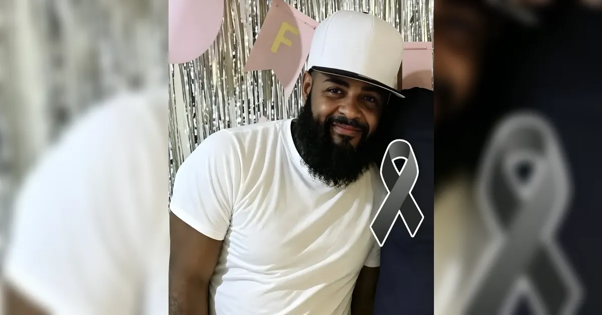 Smiling man with a white cap and white T‑shirt at a celebration, with a large gray awareness ribbon overlay.