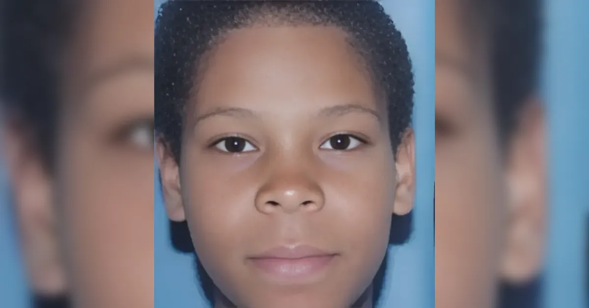 Close-up portrait of a young boy with short curly hair, facing the camera against a blue background.
