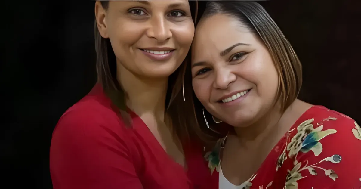 Two women smiling and hugging, wearing red tops against a dark background.08Conveys friendship and portrait context.