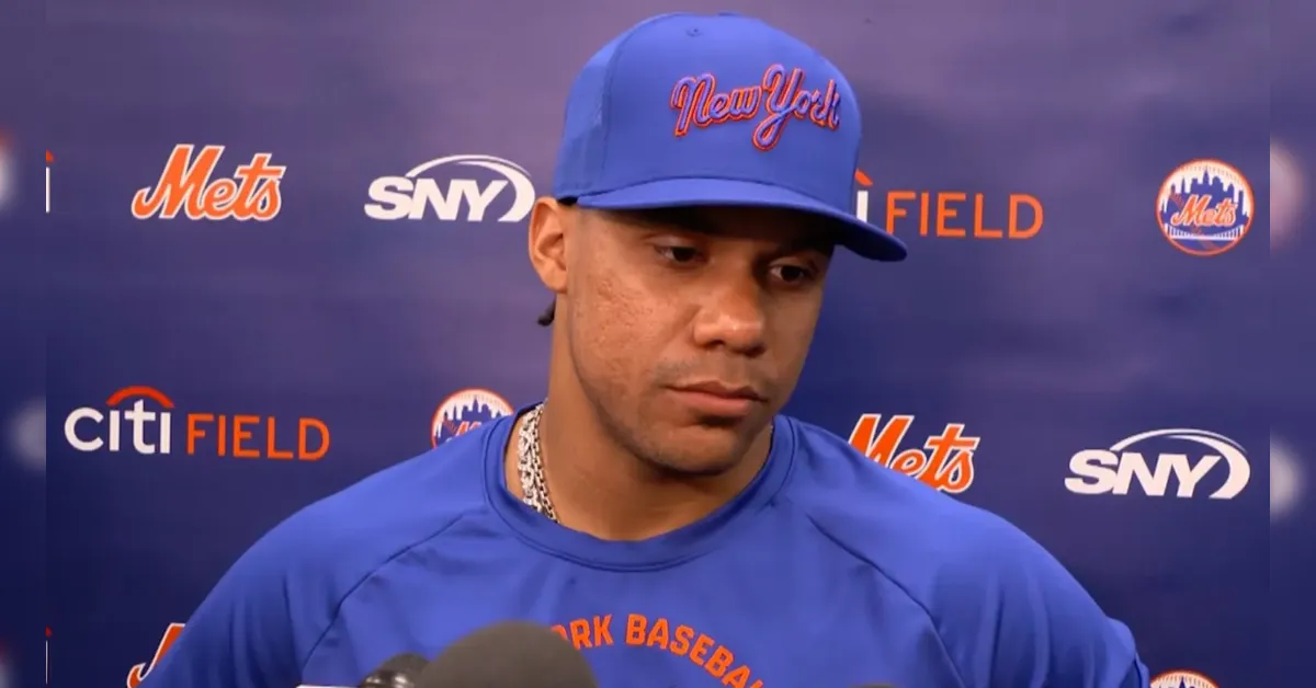 Baseball player in a blue Mets cap and jersey speaks to reporters at a Citi Field press backdrop.