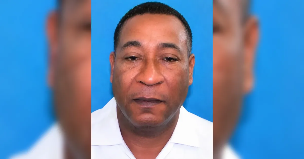 Close-up portrait of a man in a white collared shirt against a blue background, neutral expression.