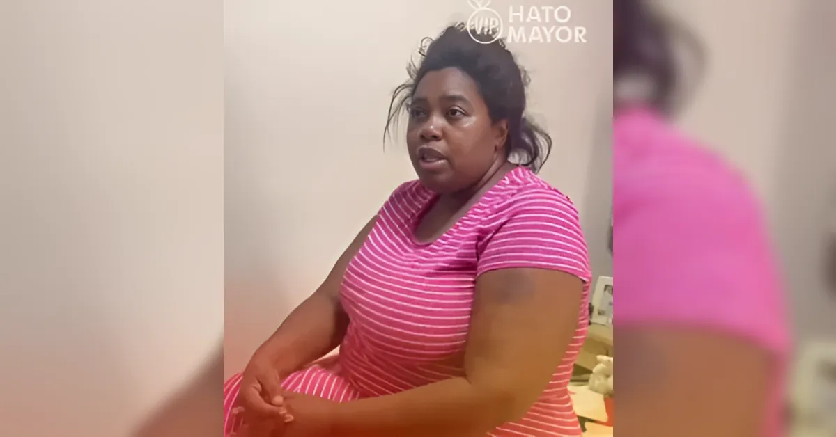 Woman in a pink striped shirt sits in a room, speaking to someone off-camera.