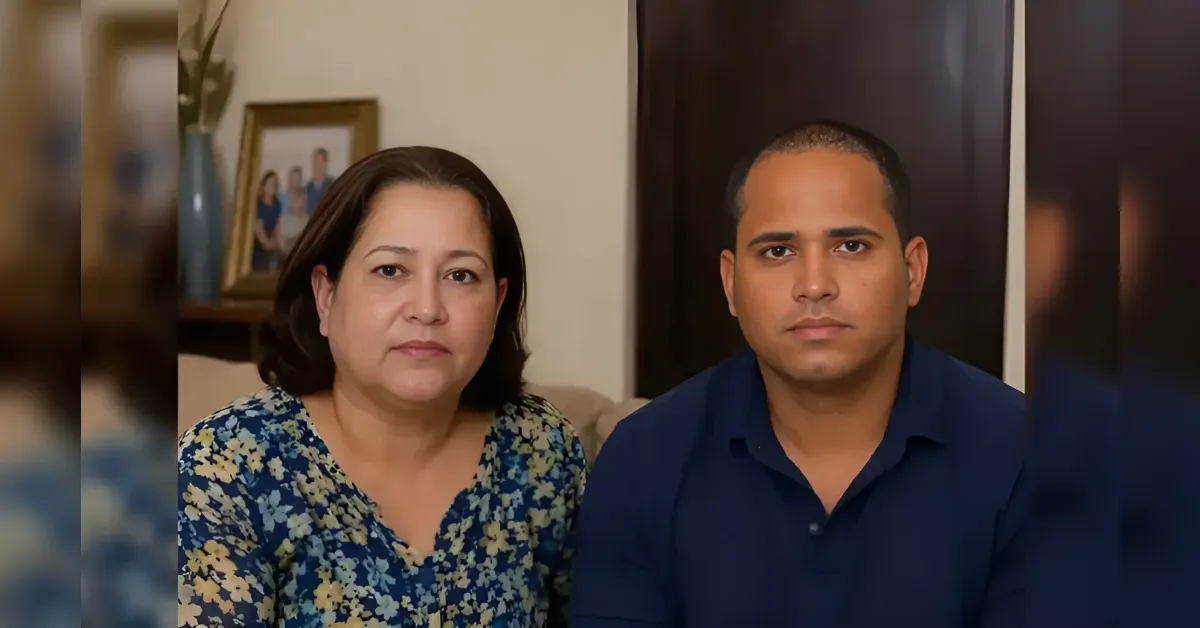 Woman and man sit side by side on a sofa in a living room, looking at the camera with neutral expressions.