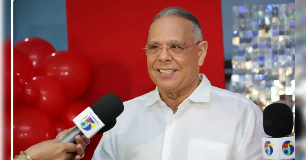 Smiling man in a white dress shirt being interviewed by reporters, two microphones in front of him.