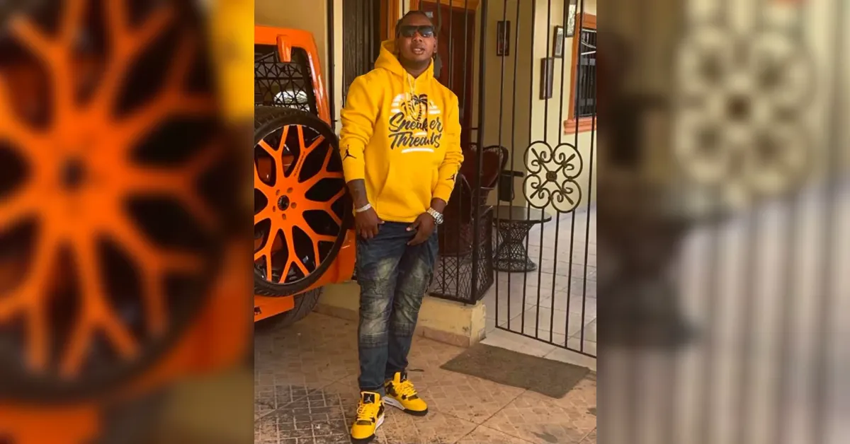 Person wearing a bright yellow hoodie with 'Sneaker Trends' text, sunglasses, and distressed jeans stands outside a doorway next to an orange wheel.