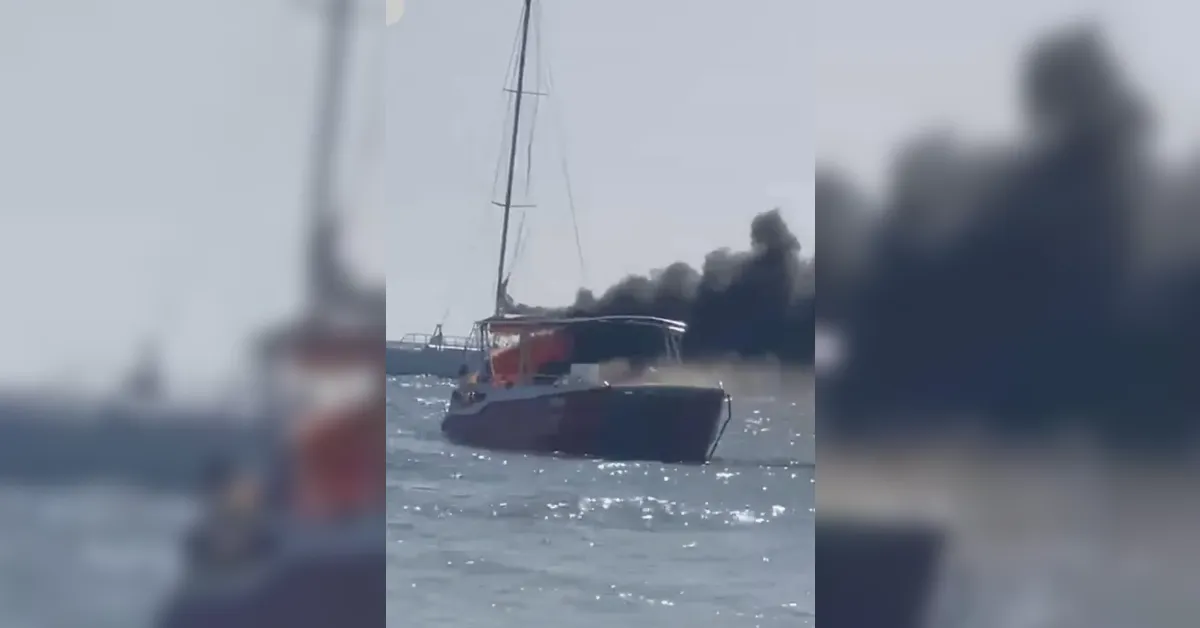 Motor yacht on the sea with a dark smoke plume rising behind it near the stern.