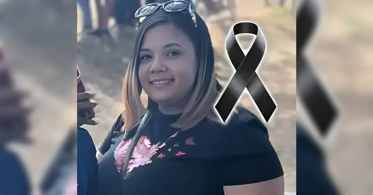 Smiling woman with shoulder-length hair wearing a black top; a large black memorial ribbon overlays the image, suggesting mourning or remembrance.