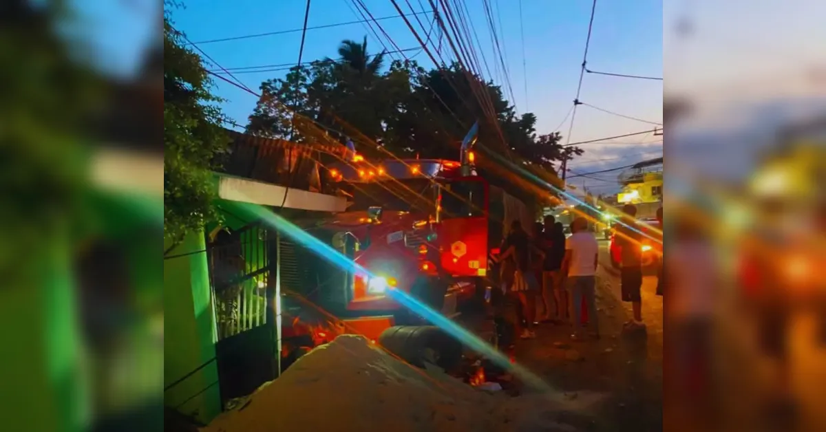 Nighttime street scene with a red fire truck and flashing lights; debris and a collapsed storefront in the foreground as bystanders watch a rescue operation near tangled overhead wires.
