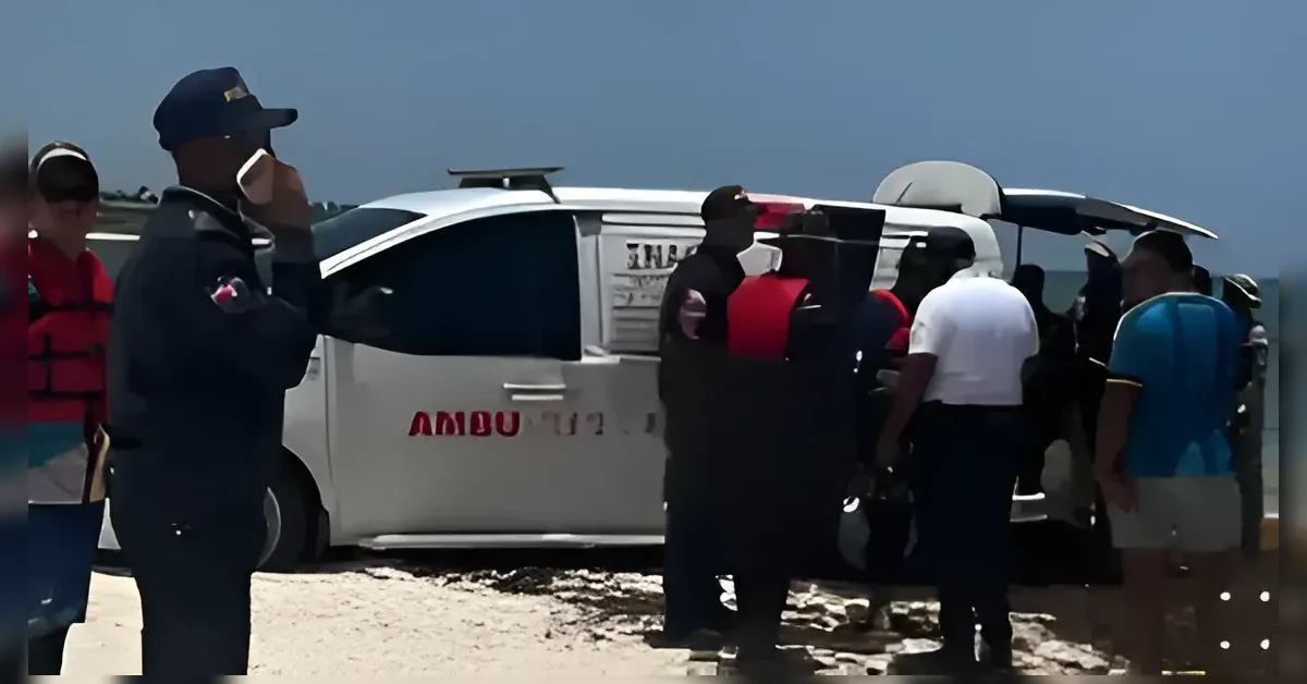 People stand on a sandy beach around a white SUV that’s on its side with the door open, some wearing life jackets or vests and looking at the vehicle.