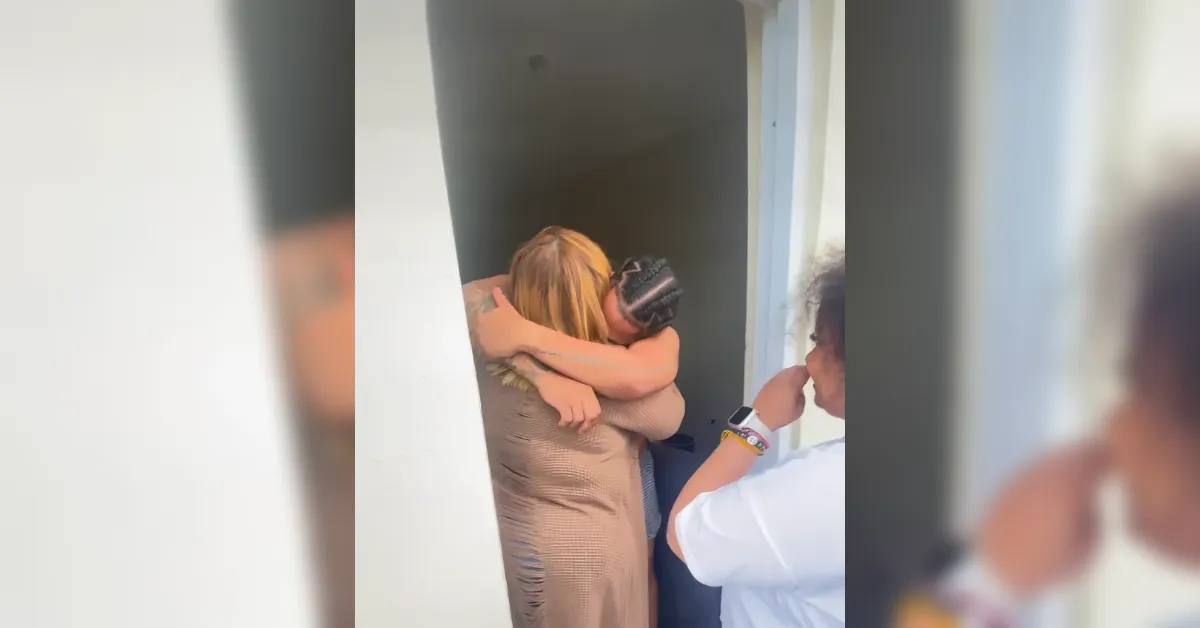 Two people share a comforting hug in a doorway as others look on from nearby.