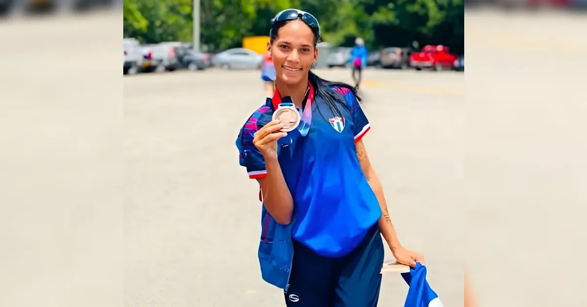 Female athlete in a blue uniform proudly holding a silver medal outdoors in a parking lot.