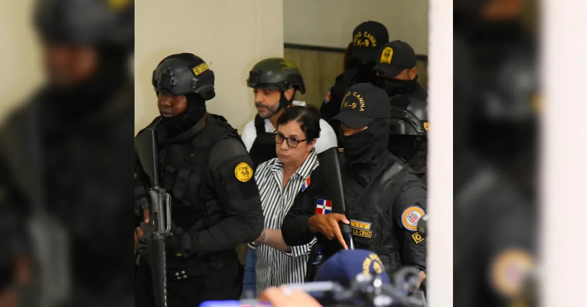 Woman in striped shirt and glasses being escorted by heavily armed police in tactical gear, with a Dominican flag patch visible.