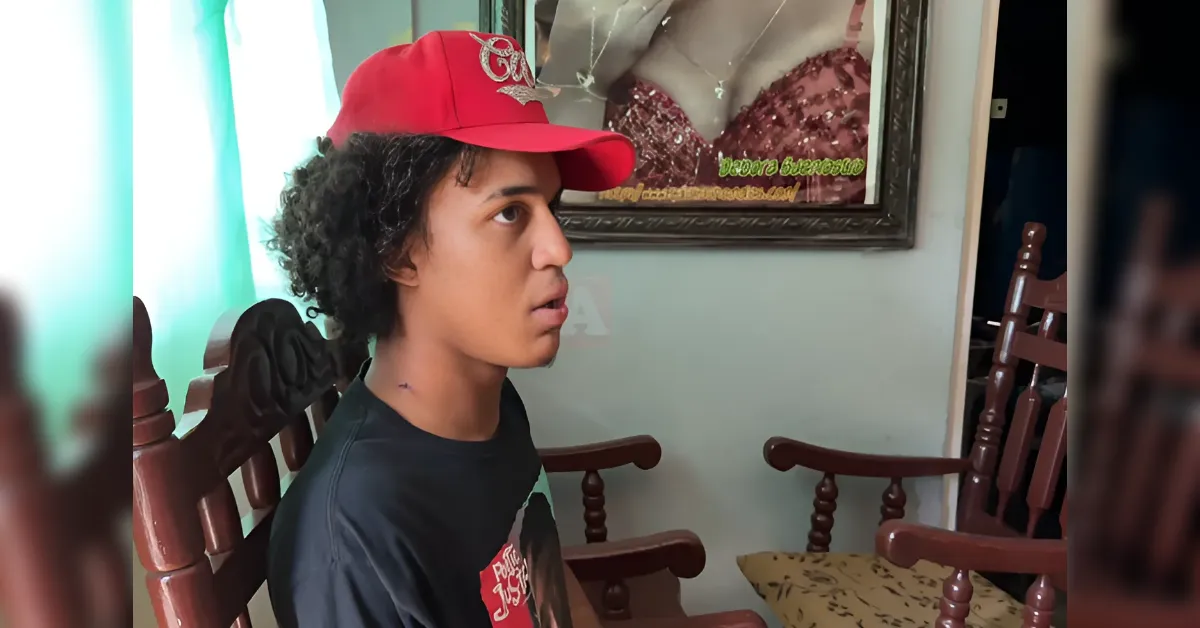 Young man wearing a red cap sits on wooden chairs indoors, looking to the left.