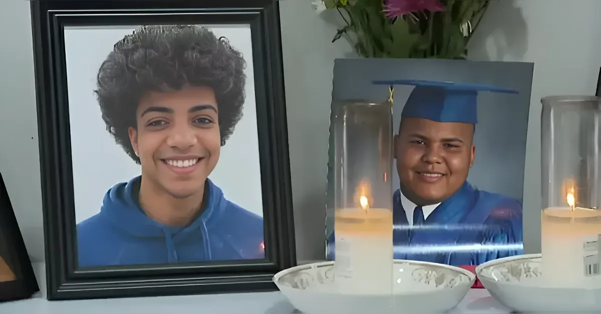 Memorial display with framed portrait of a smiling young man in a blue hoodie and a graduation photo, with candles and flowers nearby.
