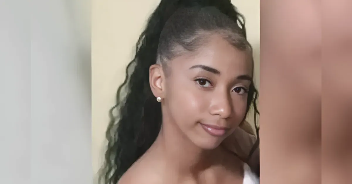 Portrait of a young woman with long, braided ponytail and pearl stud earrings, looking at the camera with a soft smile.