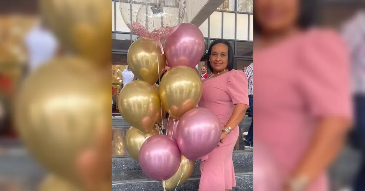Smiling woman in a pink dress posing with gold and pink balloons outside a building on steps.
