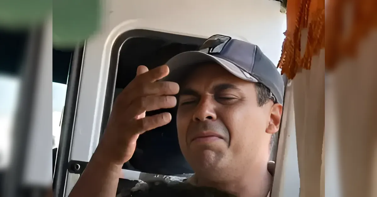 Man in a cap sits in a vehicle, eyes closed, rubbing his forehead in frustration.