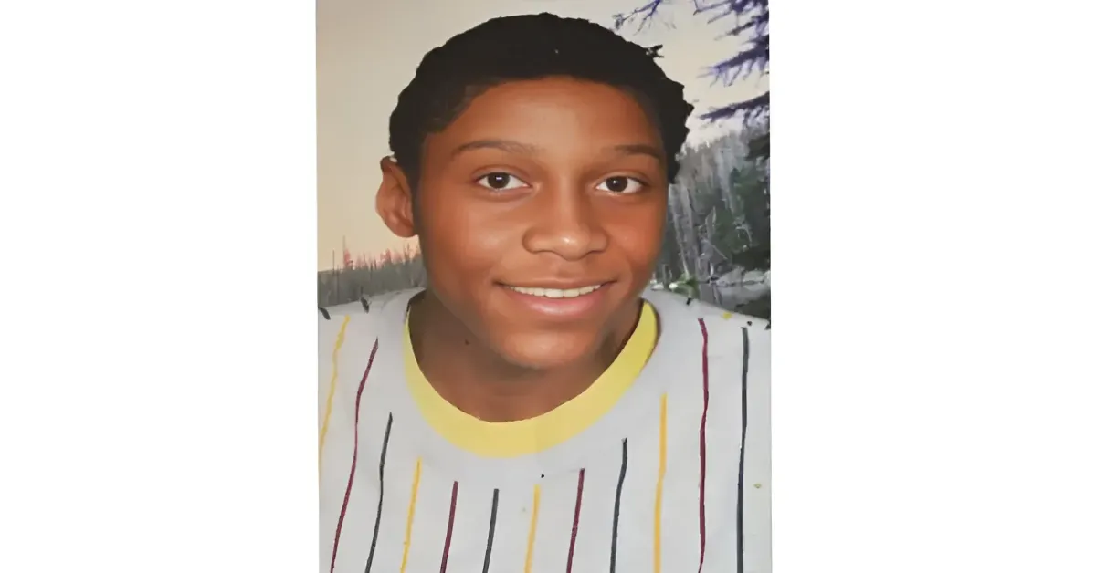 Smiling boy portrait with short, dark hair, wearing a light gray shirt with a yellow collar and vertical stripes.